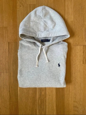 Polo Ralph Lauren Hoodie – Grå | Storlek L - Säljer en klassisk och stilsäker grå hoodie från Polo Ralph Lauren i storlek L. En mångsidig basplagg med broderad logga på bröstet som lyfter vilken outfit som helst. ✔️ Fint skick ✔️ Storlek: L ✔️ Modell: Klassisk huvtröja ✔️ Detalj: Broderad logga på bröstet  Hör gärna av dig vid frågor eller om du vill ha fler bilder. Samfraktar gärna om du kikar på mina övriga annonser! Axelbredd: 50 cm Längd: 60 cm