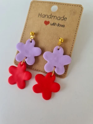 Handgjorda örhängen med retroblommor  - Unika handgjorda örhängen i form av ljuslila och orangeröda retroblommor på rad. Gjorda för hand av mig i polymerlera. 