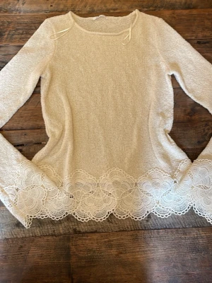 Beige topp med spetskant från Zara - Supersöt beige topp från Zara med lång ärm och dekorativ spetskant nertill. Toppen har en mjuk struktur och rund halsringning. Perfekt för dig som gillar romantiska detaljer och vill ha något extra till din outfit.