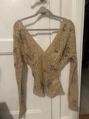 Zara topp - Supersnygg beige blus i spets med v-ringad hals och långa ärmar. Blusen har ett blommigt mönster och är figurnära med stretchigt material. Perfekt för dig som vill ha en unik och trendig topp med fina detaljer.