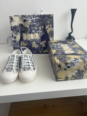 Dior sneakers med monogrammönster - Snygga låga sneakers från Dior med klassiskt grått och vitt monogrammönster. Skorna har vita snören, vit sula och 'CHRISTIAN DIOR' tryckt på tån. Tillverkade i textil med detaljer i gummi. Perfekta för dig som vill ha en exklusiv och trendig look.