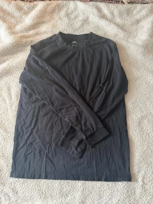Svart långärmad topp från 157 - En enkel och stilren svart långärmad topp från 157 i 100% bomull. Perfekt basplagg med rund halsringning och normal passform. Lätt att matcha med olika outfits och skön att bära hela dagen.