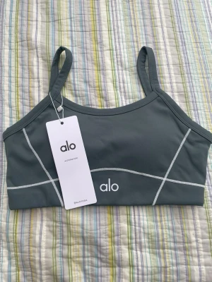 Grått sportigt set från Alo - Snyggt grått set från Alo med sport-bh och matchande tights. Setet har tunna axelband, vita kontrastsömmar och logga framtill. Materialet är stretchigt och mjukt, perfekt för träning eller chill. Tightsen har hög midja och praktiska fickor på sidorna.