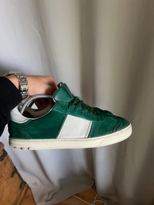 Mörkgröna Valentino Flycrew  - Snygga sneakers i mörkgrön mocka med vita läderdetaljer och vit sula. Klassisk låg modell med gröna skosnören och stilren design. Perfekta för dig som vill ha en clean och trendig look.