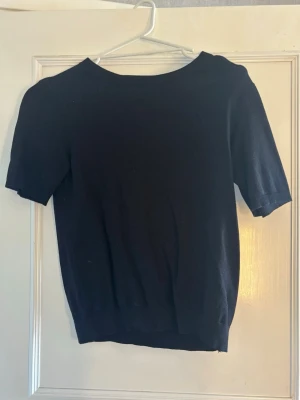 Svart kortärmad topp - En enkel svart topp med rund hals och korta ärmar. Modellen är rak och har ribbade kanter vid ärmslut och nederkant. 