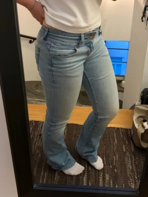 Ljusblå bootcut jeans - Säljer ett par ljusblå bootcut jeans med låg midja. Jeansen har en lätt tvättad look och är tillverkade i stretchigt denimtyg för skön passform. Perfekta för dig som gillar en avslappnad men ändå snygg stil.