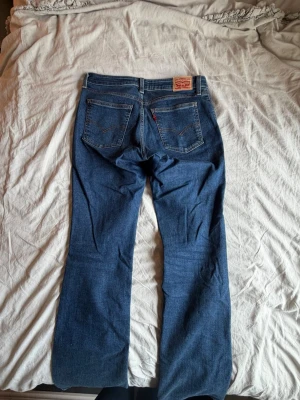 Blå Levi's bootcut jeans - Klassiska blå Levi's jeans med bootcut passform och fem fickor. Jeansen har en mörkblå tvätt, synliga sömmar och den ikoniska röda Levi's-lappen på bakfickan. As snygga o är endast använda en gång, så därav som nyskick💌