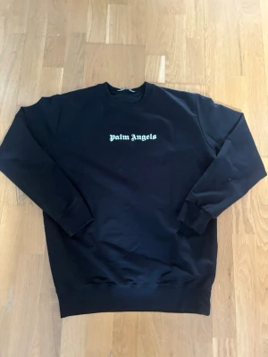 Svart Palm Angels sweatshirt - Säljer en svart sweatshirt från Palm Angels med klassisk logga i vitt på bröstet. Perfekt för dig som gillar streetwear och enkel stil. Storlek M och väldigt slim fit!! 