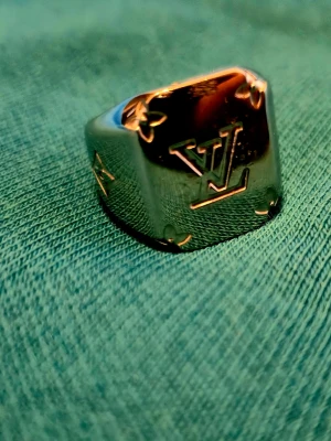 Silverfärgad Louis Vuitton ring - Stilren och chunky silverfärgad ring från Louis Vuitton med LV-logga på framsidan och stjärndetalj på sidan. Ringen har en fyrkantig form och är tillverkad i metall med blank finish. Perfekt för dig som vill ha en statement-accessoar. Riktigt ovanlig ring som jag ägt i 3 år men vuxit ifrån😅prutmån finns