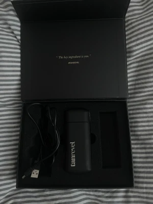 Tanrevel spraytan-apparat  - Elektronisk spraytan-apparat från Tanrevel i svart plast med vit logga. Kommer i originalförpackning med USB-laddningskabel. Smidig och portabel design, perfekt för att applicera brun utan sol jämnt och enkelt hemma.