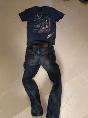 Blå t-shirt Vita di Mare - Två snygga t-shirts från Vita di Mare, en i marinblått och en i vitt, båda med tryck av vinflaska och text framtill. Klassisk rund hals och korta ärmar. Perfekt för dig som gillar stilrena tryck och vill ha en avslappnad look.