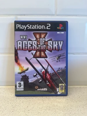 WWI Aces of the Sky PS2 spel - Säljer spelet WWI Aces of the Sky till PlayStation 2. Omslaget har ett motiv med stridsflygplan från första världskriget i luften och explosioner i bakgrunden. Spelet kommer i ett blått plastfodral och är märkt för åldersgräns 3+. Perfekt för dig som gillar flyg och action! Fungerar toppen
