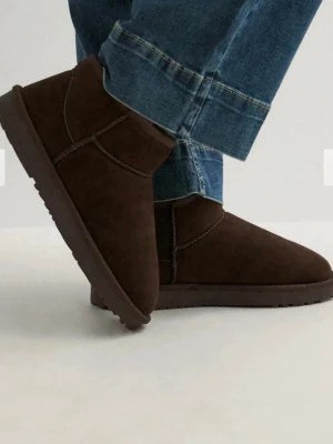 Mörkbruna fluffiga slip-in tofflor - Säljer ett par mörkbruna slip-in tofflor med mjuk och fluffig insida. Tofflorna har en klassisk rundad tå och är tillverkade i mockaliknande material. Perfekta för att hålla fötterna varma under kyliga dagar.