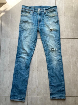 Levi Strauss & Co jeans med slitningar - Säljer ett par blåa jeans med slitningar och hål på låret och knät. Jeansen har klassisk femficksmodell, normal midja och dragkedjegylf. Materialet är denim i bomull med en tvättad look och ljusa partier. Sitter otroligt bra på, vid frågor och funderingar skriv gärna. Strl 31/32.