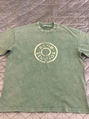 Grön t-shirt från Acne Studios - Säljer en grön t-shirt från Acne Studios med ett stort, slitet tryck i vitt på bröstet. T-shirten har rund hals och korta ärmar. Perfekt för dig som gillar en avslappnad och trendig stil.