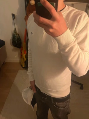 Vit sweatshirt från GANT - Snygg vit sweatshirt från GANT med rund halsringning och diskret logga på bröstet. Tröjan har ribbade muddar vid ärmslut och nederkant, vilket ger en klassisk och stilren look. Perfekt för en avslappnad och trendig stil.