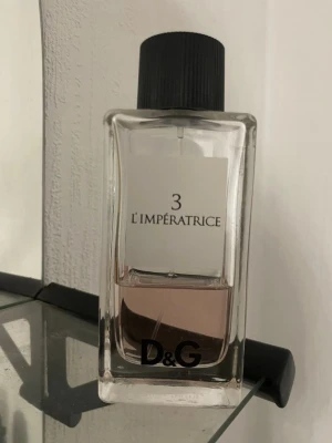 D&G 3 L'Impératrice parfym - D&G 3 L'Impératrice är en elegant parfym i en genomskinlig glasflaska med svart skruvkork. Doften har en ljusrosa vätska och flaskan har en stilren, modern design med tydlig logga och etikett framtill.