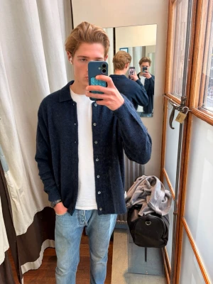 Mörkblå stickad cardigan - Säljer en mörkblå stickad cardigan med knappar framtill och klassisk krage. Tröjan har en avslappnad passform och långa ärmar, perfekt att slänga över en t-shirt. Storlek: M. Nypris 2499kr.  Material: 13% Mohair 35% Ull 49% Nylon 3% Spandex. Använd en gång!