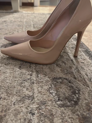 Nude lackpumps med spetsig tå - Säljer ett par stilrena pumps i nude färg med hög klack och spetsig tå. Skorna är i glansigt lackmaterial och har en klassisk, elegant siluett som passar till många olika outfits. Perfekta för dig som vill ha ett par tidlösa och trendiga klackar.