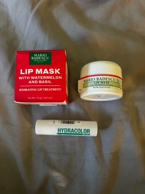 Mario Badescu Lip Mask & Hydracolor - Säljer ett Mario Badescu Lip Mask med vattenmelon och basilika i en vit rund burk och röd förpackning, samt ett vitt Hydracolor läppbalsam i stiftform, nyans 22. Perfekt för återfuktade och mjuka läppar. Helt nytt