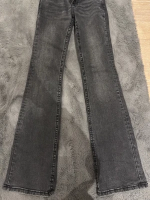 Grå bootcut jeans med fickdetalj - Säljer ett par grå bootcut jeans med snygg tvätt och markerade sömmar. Jeansen har en unik fickdetalj bak med knapp och breda hällor. Perfekta för dig som gillar en avslappnad men trendig look.