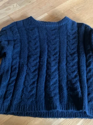 Mörkblå kabelstickad tröja 157 - Mysig mörkblå kabelstickad tröja från 157 i storlek XS. Tröjan har ett klassiskt flätmönster, rund halsringning och är gjord i ett mjukt material som passar perfekt för kyliga dagar. Enkel att matcha till både jeans och kjol.