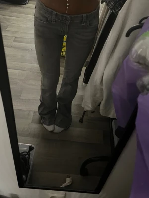 Grå bootcut jeans med låg midja - Säljer ett par gråa bootcut jeans med låg midja och klassiska fem fickor. Jeansen har en snygg tvättad look och är perfekta för dig som gillar en avslappnad men trendig stil. Materialet känns som bomullsdenim och passformen är figurnära upptill och utsvängd nedtill.