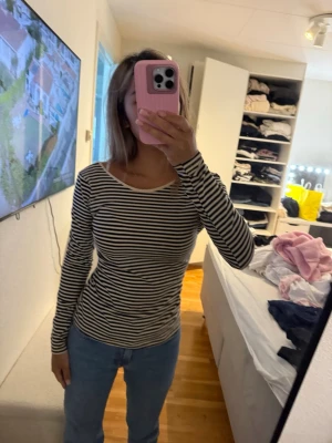 Randig långärmad topp i bomull och öppen rygg  - Snygg långärmad topp med svartvita ränder och rund halsringning med öppen rygg. Modellen är figurnära och passar perfekt till jeans eller kjol. Tillverkad i mjuk bomull som känns skön mot huden. Enkel och stilren design som funkar till många olika looks.