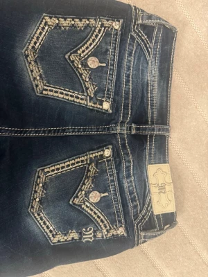 Mörkblå jeans med broderade fickor - Snygga mörkblå jeans med slitningar och detaljerade broderier samt paljetter på bakfickorna. Perfekta för dig som gillar unika detaljer och vill sticka ut lite extra. 