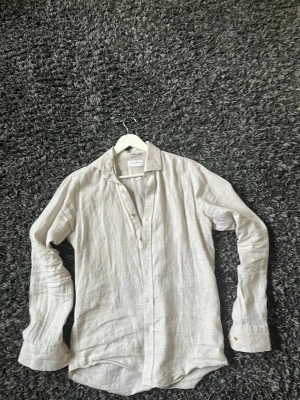 Beige linneskjorta från John Henric - Säljer en stilren beige skjorta från John Henric i 100% linne. Skjortan har klassisk krage, knappar framtill och långa ärmar. Perfekt för dig som gillar en avslappnad men ändå snygg look. Så gott som nyskick, använd ett par gånger. Den passar som mellan S och M. Skriv gärna era frågor!