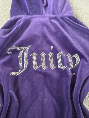Juicy Couture zip hoddie💜✨ - Säljer en fin Juicy Couture zip hoodie i storlek XXS. Perfekt för en söt och bekväm look. 💕Nypris: över 1200 ✨ Märke: Juicy Couture ✨ Färg: Lila ✨ Storlek: XXS ✨ Modell: Zip hoodie ✨ Skick: Har några mindre skador och ett par fläckar. Fläckarna kan eventuellt försvinna i tvätten. I övrigt fortfarande i fint och fullt användbart skick. Rollas och tvättas självklart av innan skickning, men ber om ursäkt för eventuella katthår. 🫶 Hör gärna av dig om du har frågor eller vill ha fler bilder! 💕