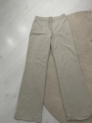Beige mjukisbyxor med raka ben - Säljer ett par beige mjukisbyxor från 157 med raka ben och dragsko i midjan. Byxorna har resår i midjan och sidofickor. Perfekta för chill dagar eller när du vill ha det extra bekvämt.