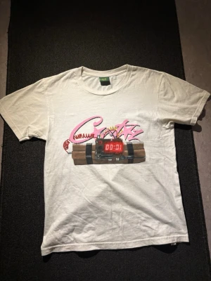 CORTIZ NO TIME 4 LUV T-shirt  - Vit t-shirt med coolt tryck framtill som föreställer en digital bomb med färgglada sladdar och rosa graffiti-text. Klassisk passform och rund halsringning. Perfekt för dig som vill sticka ut med en unik och edgy stil.
