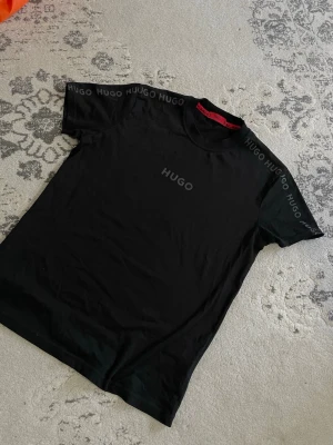 Hugo boss - Snygg svart t-shirt från HUGO med diskret logga på bröstet och HUGO-tryck längs axlarna. Klassisk rund halsringning och korta ärmar. Perfekt basplagg med stilren design och skön passform.