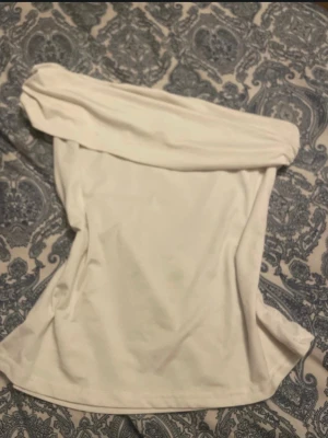 Vit offshoulder topp från SHEIN - Snygg vit offshoulder topp från SHEIN i stretchigt material. Toppen är axelbandslös och har en bred kant upptill som ger en trendig look. Perfekt att styla med jeans eller kjol för en cool outfit.