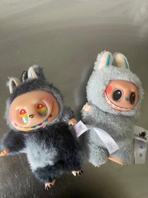 Två fluffiga monster-gosedjur - Säljer två unika gosedjur med stora färgglada ögon och fluffiga dräkter. Ena har mörkgrå päls med vita öron och den andra ljusgrå päls med blå detaljer. Båda har gulliga ansikten och små tassar. Perfekt för dig som gillar samlarfigurer eller vill ha något annorlunda i rummet.
