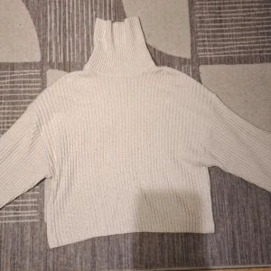 Beige polotröja från H&M - Stickad beige polotröja från H&M med bred ribbstickning och hög krage. Tröjan har en avslappnad passform och långa ärmar, perfekt för kalla dagar. Enkel och stilren design som passar till det mesta.