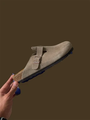 Birkenstock Boston i mocka st 42 - Säljer ett par Birkenstock i mocka med klassiskt spänne på ovansidan. Yttersulan är svart med mönstrad struktur och innersulan är i kork. Perfekt för dig som gillar stilrena och bekväma skor.