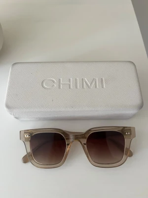 Chimi solglasögon 04 Ecru - Snygga solglasögon från CHIMI med transparent beige båge och fyrkantig form. Glasen är bruna med snygg toning. Perfekta för soliga dagar och ger en modern vibe till din outfit. Kommer med originaletui.
