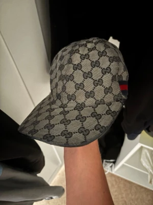 Gucci Navy Canvas GG - Snygg keps från Gucci i grått med klassiskt GG-monogram över hela kepsen. På sidan finns en svart och röd rand som ger extra stilpoäng. Kepsen har böjd skärm och är tillverkad i ett tygmaterial som känns lyxigt och trendigt. Pris går att diskuteras, kepsen är felfri förutom att knappen där uppe 👆 saknas tyvärr, Hör av er med bud eller om ni vill ha mer bilder! 😁Box och tillbehör går att lösa! Mvh Zion✌️