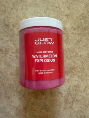 Just Glow Watermelon Explosion Body Scrub - Sockerbaserad body scrub med doft av vattenmelon från Just Glow. Innehåller sheasmör och vitamin E för extra återfuktning. Vegansk och tillverkad i Sverige. Oanvänd och plomberad. 