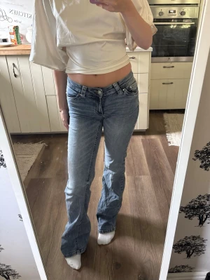 Blå bootcut jeans med låg midja - Säljer ett par ljusblå bootcut jeans med låg midja och klassisk femficksmodell. Jeansen har en lätt tvättad look och raka ben som går ut lite nedtill. Perfekta för dig som gillar en avslappnad och trendig stil.