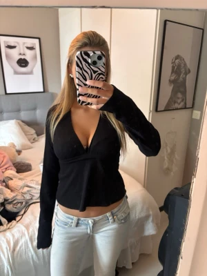 Svart omlottopp med knytband - Snygg svart omlottopp med djup v-ringning och långa ärmar. Toppen har knytband i midjan som ger en smickrande passform. Perfekt till jeans eller kjol för en trendig look.