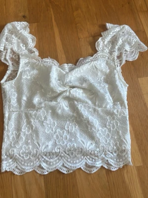 Vit spetsblus från SHEIN XS - Supersöt vit blus från SHEIN i storlek XS. Toppen är i spets med blommigt mönster, volangiga ärmar och vacker scallop-kant nertill. Perfekt för dig som gillar romantisk och feminin stil.
