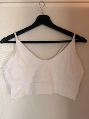 Vit ribbad crop top med smala band - Säljer en enkel och stilren vit crop top i ribbat material. Toppen har smala axelband och en mjuk, stretchig passform som sitter skönt mot kroppen. Perfekt att bära under skjortor eller som den är till jeans eller kjol.