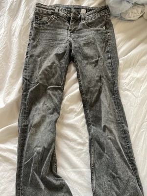 Grå bootcut jeans med tvättad look - Säljer ett par grå bootcut jeans med tvättad finish och klassisk femficksmodell. Jeansen har normal midja och raka ben som går ut lite nedtill. Materialet är mjukt denim som sitter bekvämt och passar perfekt till en avslappnad stil. 
