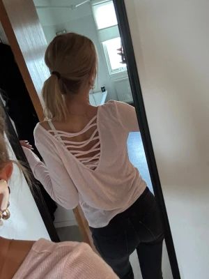 Rosa långärmad topp med öppen rygg - Säljer en rosa långärmad topp i tunn bomull med snygg öppen rygg och snörningsdetaljer. Toppen har en avslappnad passform och är perfekt för dig som gillar unika detaljer på dina plagg.