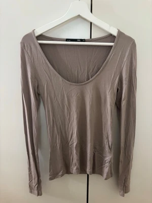 Beige långärmad topp - Säljer en beige långärmad topp från 157 med djup rundad ringning. Toppen är i ett mjukt och stretchigt material, perfekt för att styla med jeans eller kjol. Enkel och stilren design som passar till många olika looks.