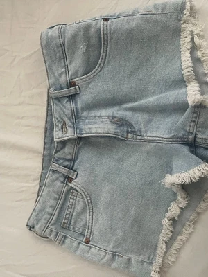 Ljusblå jeansshorts med fransar - Säljer ett par ljusblå jeansshorts med fransiga kanter. Är storlek 40 passar nån som har 36 i storlek med är som nya nästan aldrig använda.