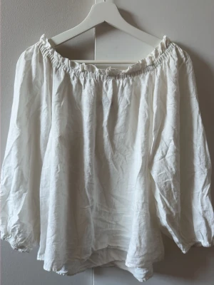 Vit offshoulder blus från Lindex - Säljer en vit offshoulder blus från Lindex i storlek S. Blusen har långa, luftiga ärmar och är gjord i ett lätt, skrynkligt tyg som ger en avslappnad vibe. Perfekt till jeans eller kjol för en trendig look.